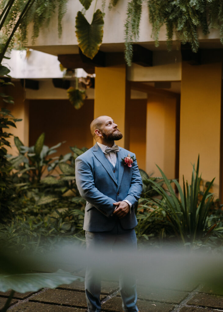 groom looking up, standing with his hands clasped in front of him, wearing light blue suit