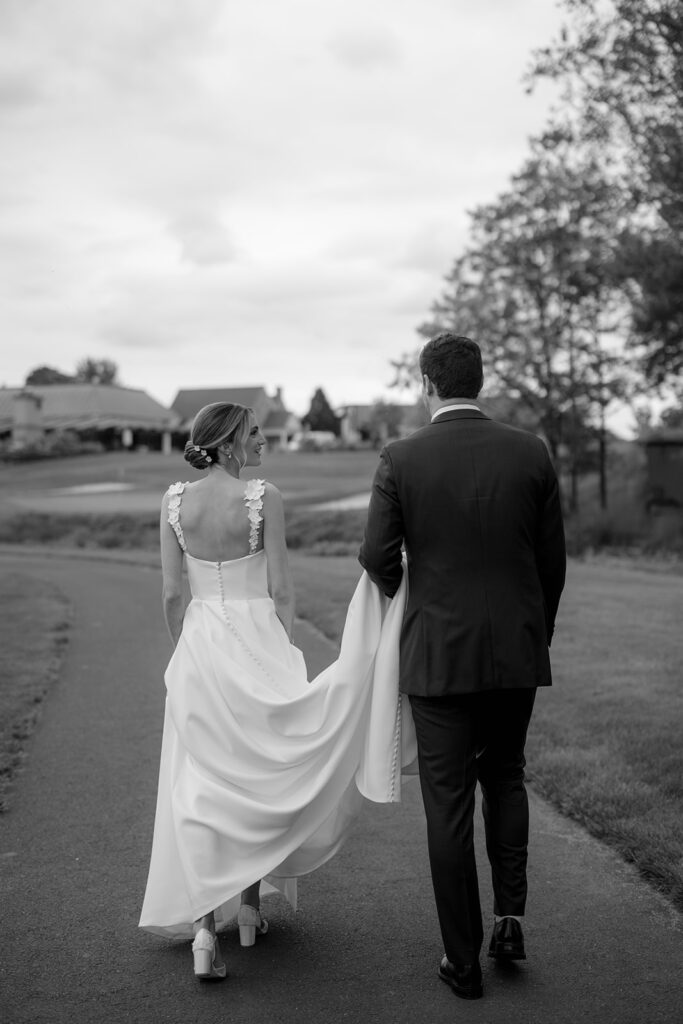 Black and white photo of a bride and groom walking away from the camera while groom is holding the brides train shot by the timeless wedding photographer Monika Eisenbart