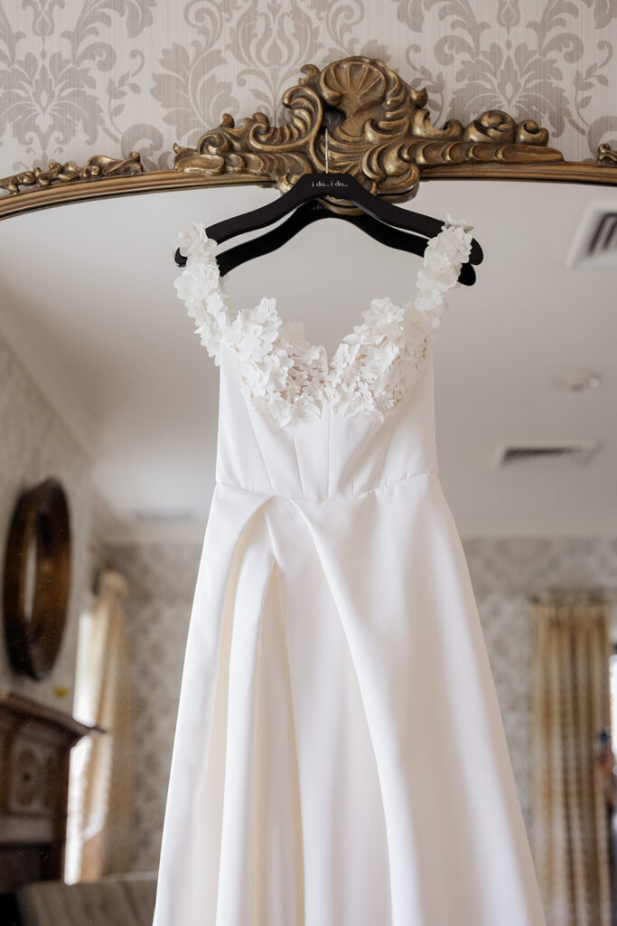 Beautiful wedding dress hanging off large ornate mirror shot by the timeless wedding photographer Monika Eisenbart