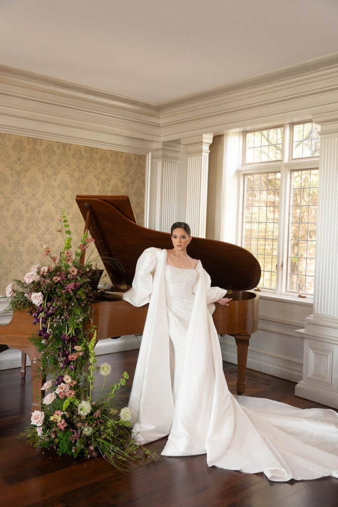 gorgeous bride leaning against piano adorned with flowers in european inspired wedding editorial