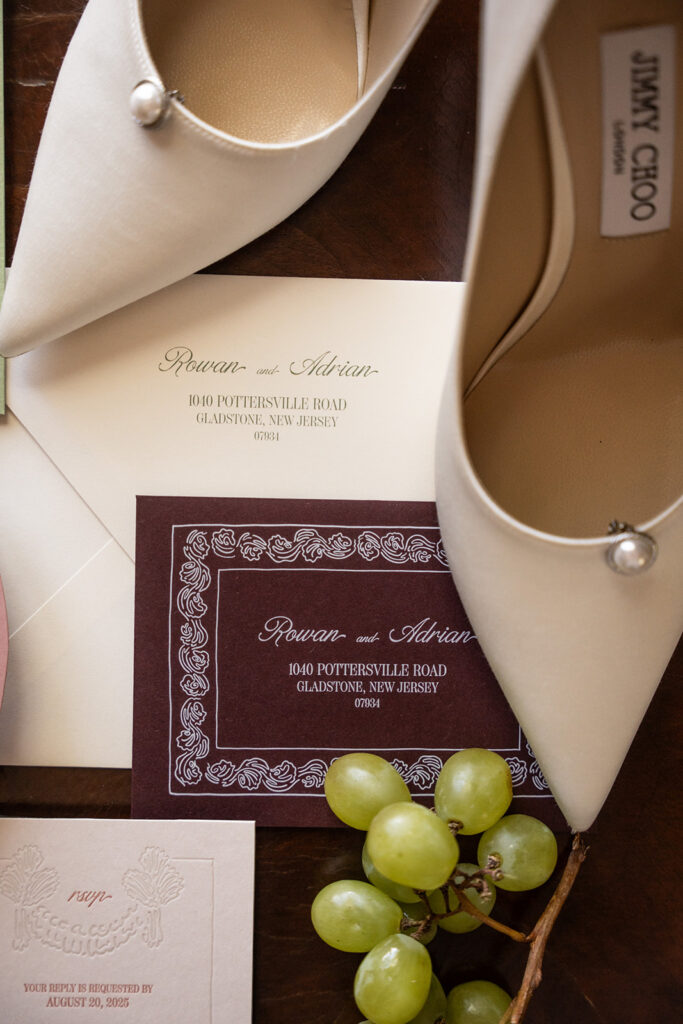 Flat lay of wedding stationery designed by the Gold Edit, featuring grapes, Jimmy Choo pumps and letterpress paper